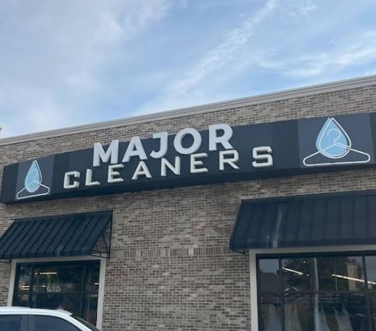 Storefront for Major Cleaners with black awning, brick exterior, and sign featuring water droplet logos with hangers.
