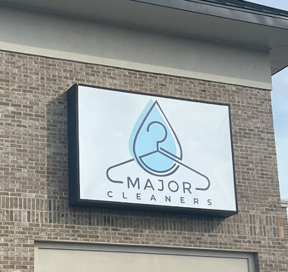 A sign on a brick building displays the logo and name "Major Cleaners" with a blue water droplet and hanger graphic.
